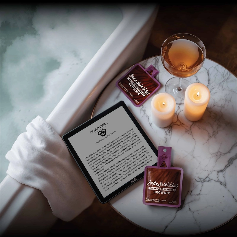 Elegant spa scene with BakeSale Vibes products, amber beverage, lit candles, and tablet on marble surface creating luxurious relaxation atmosphere